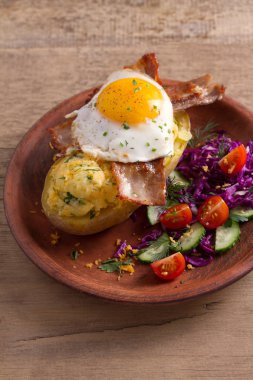 Ceketli fırında patates peynir ile yüklenen ve pastırma ile tepesinde ve sebze ile plaka üzerinde yumurta kızarmış. Tepesi ile doldurulmuş patates 