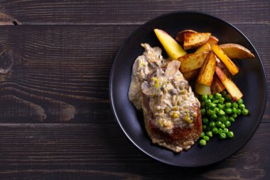 Sığır eti biftek diane ile mantar ve pırasa krema sos, patates kızartması ve yeşil bezelye plaka ahşap arka plan üzerinde siyah. ek yük