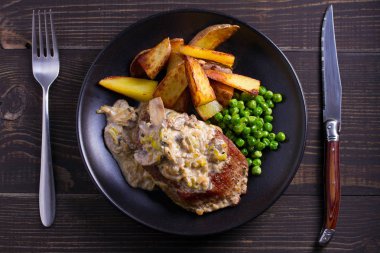 Sığır eti biftek diane ile mantar ve pırasa krema sos, patates kızartması ve yeşil bezelye plaka ahşap arka plan üzerinde siyah. ek yük