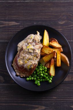 Sığır eti biftek diane ile mantar ve pırasa krema sos, patates kızartması ve yeşil bezelye plaka ahşap arka plan üzerinde siyah. ek yük