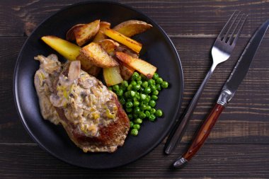 Sığır eti biftek diane ile mantar ve pırasa krema sos, patates kızartması ve yeşil bezelye plaka ahşap arka plan üzerinde siyah. ek yük