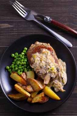 Sığır eti biftek diane ile mantar ve pırasa krema sos, patates kızartması ve yeşil bezelye plaka ahşap arka plan üzerinde siyah. ek yük