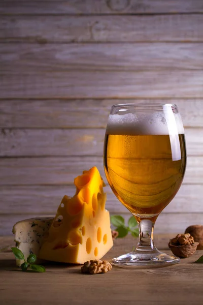 Beer and cheese. Beer glass on wooden table. Ale and appetizer snack. vertical