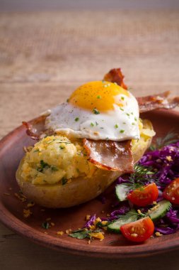 Fırında patates ceketli çedar peyniri ile yüklenen ve pastırma ile tepesinde ve ahşap masa tabakta Yumurta kızarmış. dikey