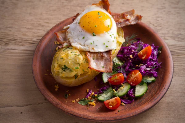 Fırında patates ceketli çedar peyniri ile yüklenen ve pastırma ile tepesinde ve ahşap masa tabakta Yumurta kızarmış. Yatay