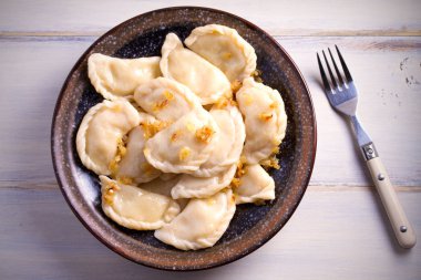 Pierogi veya pyrohy, varenyky, vareniki, köfte ahşap masa üzerinde kasede karamelize salamura soğan ile devam eder. Yatay