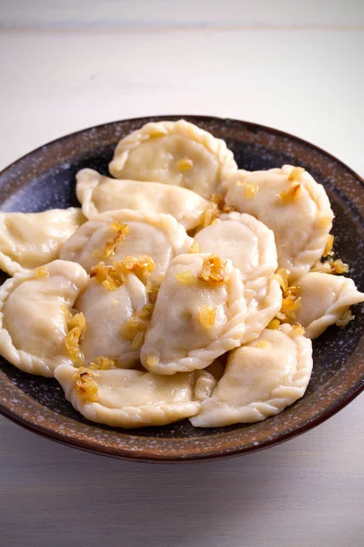 Pierogi veya pyrohy, varenyky, vareniki, köfte ahşap masa üzerinde kasede karamelize salamura soğan ile devam eder. dikey