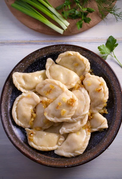 Pierogi veya pyrohy, varenyky, vareniki, köfte ahşap masa üzerinde kasede karamelize salamura soğan ile devam eder. dikey