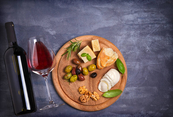 Bottle and glass of wine with cheese, olives, bread, nuts and basil on dark background. Wine and food concept. View from above, top