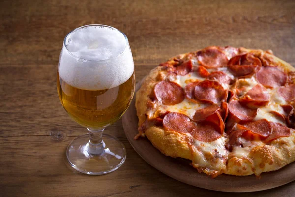 Beer and pepperoni pizza on wooden table. Glass of beer. Ale and food concept. horizontal