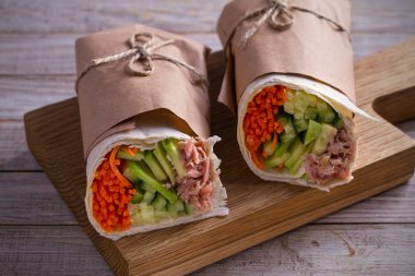 Homemade tasty burrito with tuna fish, cucumber, avocado and carrot. Tuna wraps on wooden background. horizontal clipart