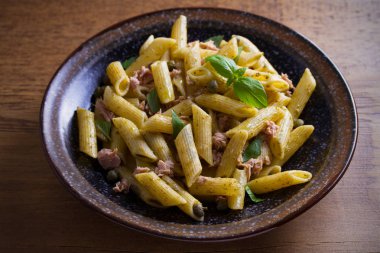 Ton balığı, fesleğen ve Kapari penne pesto sos kase ahşap arka plan ile. Ton balıklı makarna. Tepegöz, yatay