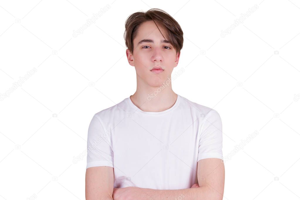 Confident serious young man keeping arms crossed. Handsome teen boy looking at camera. Portrait of teenager in white T-shirt, isolated on white background
