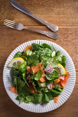 Füme somon ıspanak turp salatalık salatası ahşap masa üzerinde beyaz tabakta limonlu. Tepegöz, dikey