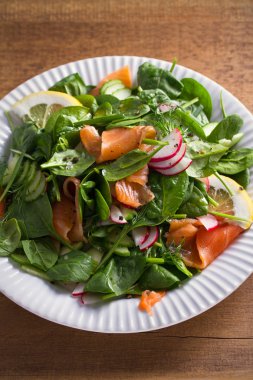 Füme somon ıspanak turp salatalık salatası ahşap masa üzerinde beyaz tabakta limonlu. dikey