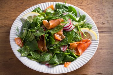 Füme somon ıspanak turp salatalık salatası ahşap masa üzerinde beyaz tabakta limonlu. Yatay