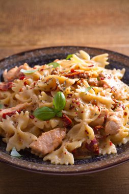 Makarna tavukla, domates ve fesleğen ahşap masa üzerinde bir kapta krem mozzarella soslu kurutulmuş. dikey 