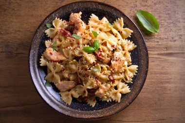 Makarna tavukla, domates ve fesleğen ahşap masa üzerinde bir kapta krem mozzarella soslu kurutulmuş. Tepegöz, yatay 