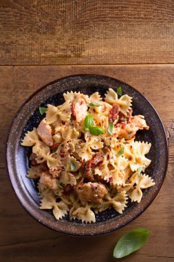 Makarna tavukla, domates ve fesleğen ahşap masa üzerinde bir kapta krem mozzarella soslu kurutulmuş. Tepegöz, dikey 