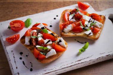 Caprese Bruschetta beyaz rustik doğrama tahtası üzerinde. Domates, fesleğen, mozzarella peyniri tost balsamik soslu. Meze - starter çanak. Yatay
