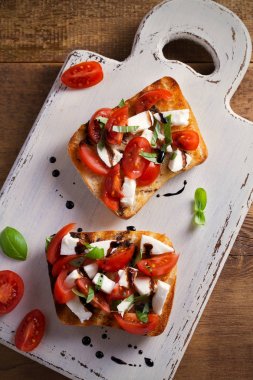 Caprese Bruschetta beyaz rustik doğrama tahtası üzerinde. Domates, fesleğen, mozzarella peyniri tost balsamik soslu. Meze - starter çanak. Tepegöz, dikey