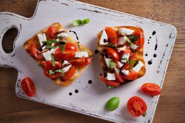 Caprese Bruschetta beyaz rustik doğrama tahtası üzerinde. Domates, fesleğen, mozzarella peyniri tost balsamik soslu. Meze - starter çanak. Tepegöz, yatay