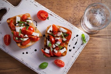 Caprese Bruschetta beyaz rustik doğrama tahtası üzerinde. Domates, fesleğen, mozzarella peyniri tost balsamik soslu. Meze - starter çanak. Tepegöz, yatay