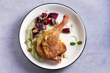 Kızarmış ördek bacağı, yeşil sebze püresi, pancar kökü ve açık gri arka planda balkabağı çekirdeği. Genel Görüntü