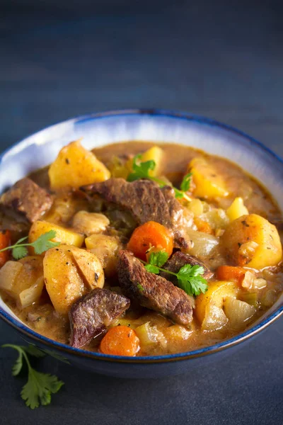 Beef meat stewed with potatoes, carrots and spices in bowl on dark gray background. vertical image
