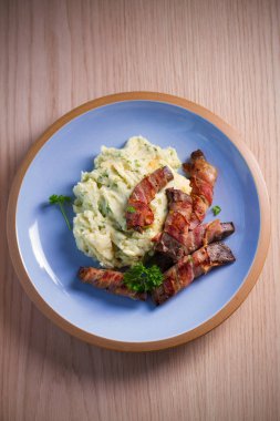 Domuz pastırmasına sarılı sığır ciğeri ve mavi masada patates püresi. Tepedeki dikey resim