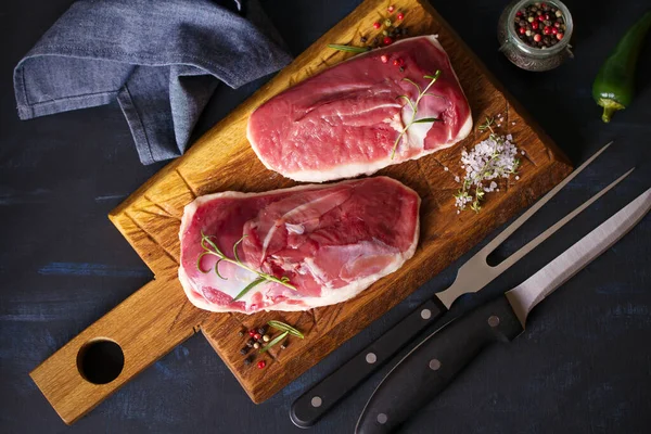 Raw fresh meat, duck breast fillet on wood chopping board with rosemary and seasons. Flat lay