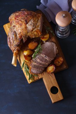 Roast leg of lamb with potatoes and rosemary on serving wooden board. View from above, top view clipart