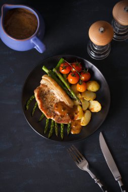 Siyah tabakta sebzeli domuz pirzolası. Tepedeki dikey resim