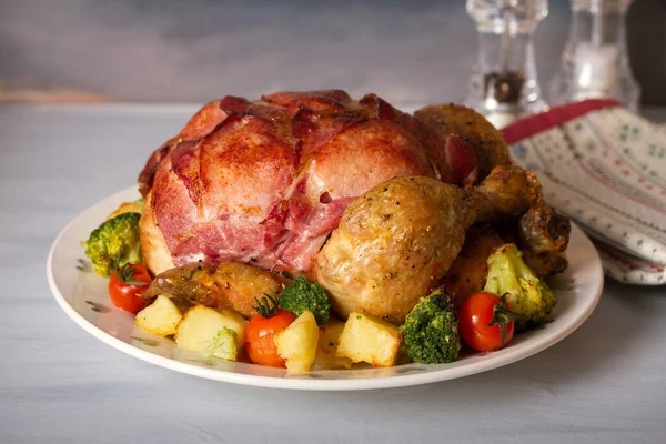 Whole roast chicken with breasts wrapped in bacon and vegetables: potatoes, broccoli and tomatoes. horizontal image