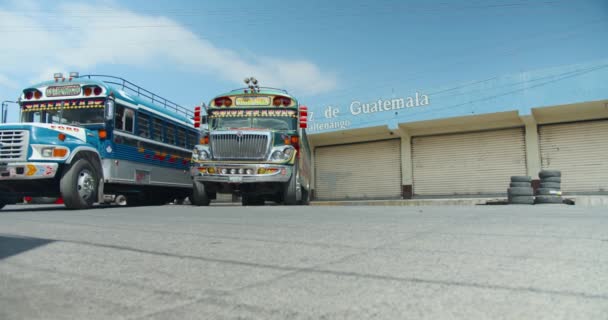 Zwei Hühnerbusse fahren in Xela mit stehendem Bus und Guatemala-Schild dicht auf — Stockvideo