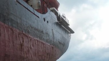 Kuru bir kargo gemisinin buruşmuş siyah kırmızı demir tarafı, bulutlu bir günde pencerelerinde ipler asılı.