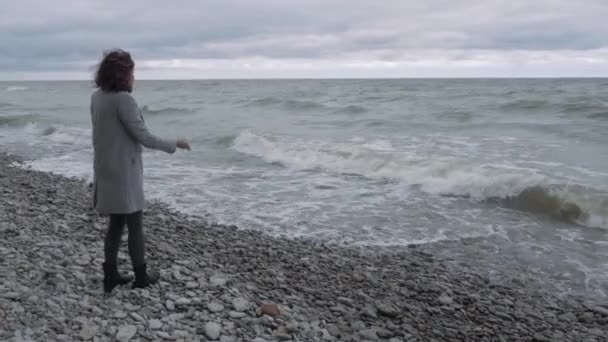 Сумна Дівчина Сірому Пальто Стоїть Кам Яному Пляжі Кидає Гальку — стокове відео