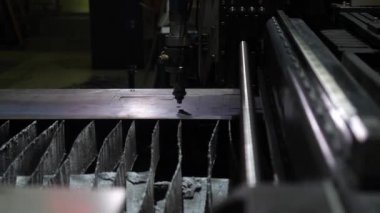 Yetersiz aydınlatılmış bir odada daha fazla kıvılcımla otomatik lazer kesimi, makine karanlık bir arkaplanda açık bir robot hareketi yapar.