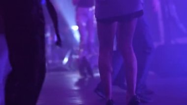 Kısa etekli, yüksek topuklu genç bir kızın güzel çıplak bacakları kalabalığın arasında bir gece kulübünde müzik eşliğinde dans ediyor.