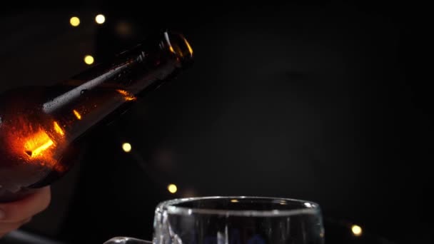 在黑色的背景下 冷的金色啤酒慢慢地从一个薄薄的瓶子中倒入一个杯子 — 图库视频影像