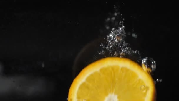 tranche d'orange tombe dans l'eau avec des bulles, éclaboussures et mousse sur un fond noir 180fps 