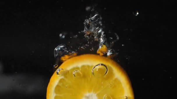 Szelet Narancs Esik Vízbe Buborékok Fröccsenések Hab Fekete Alapon 180Fps — Stock videók