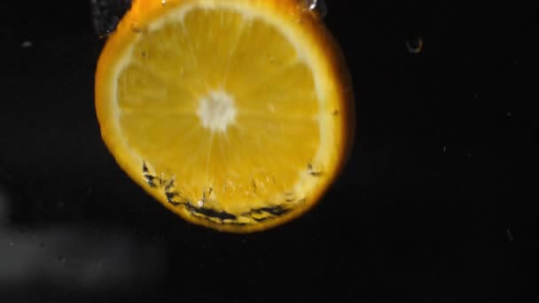 tranche d'orange tombe dans l'eau avec des bulles, éclaboussures et mousse sur un fond noir 180fps 
