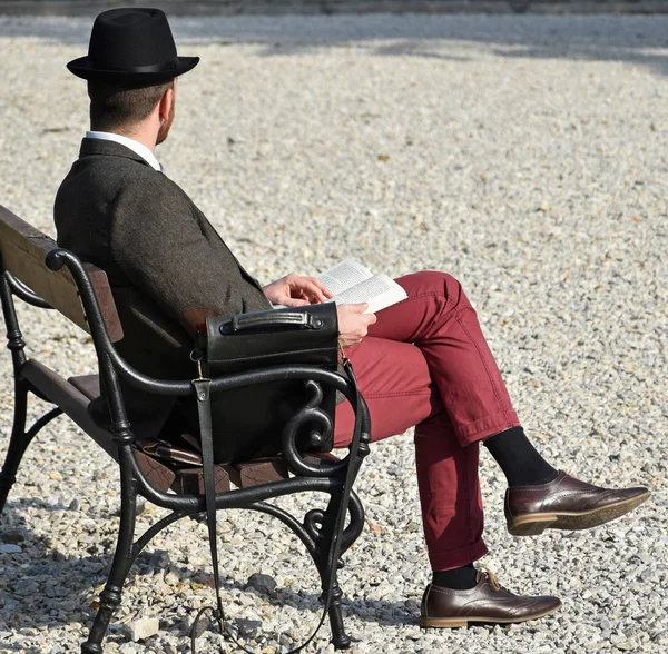 Man is sitting on a park bench and reading — Stock Photo, Image