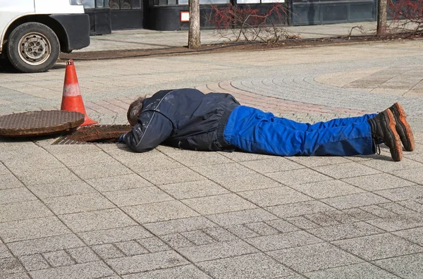 El hombre está trabajando al lado de una tapa de alcantarilla — Foto de Stock