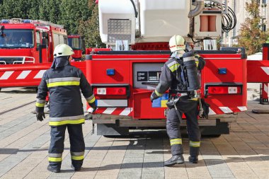 İtfaiyeciler itfaiye arabasının yanında.