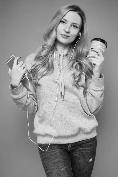 Söt positiva blond kvinna i hoodie med telefon och kaffe — Stockfoto