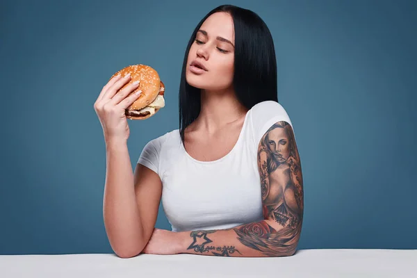 Linda menina tatuagem encantadora segurando hambúrguer — Fotografia de Stock