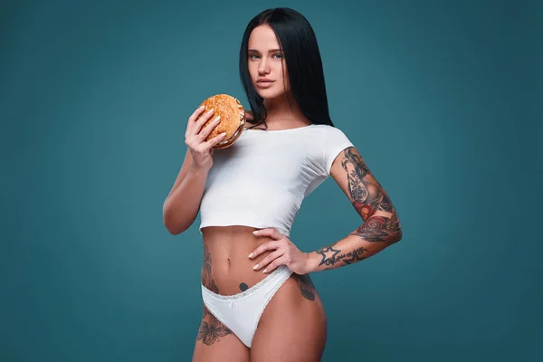 Beautiful charming tattoo girl holding hamburger — Stock Photo, Image