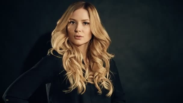 Blondýnka s kudrnatými vlasy pózuje na černém pozadí v studio — Stock video